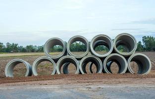 Low angle view, large concrete pipes lined up, stacked on top of the ground beside the paved road. photo