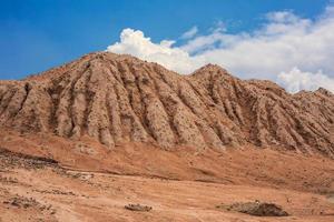 A large mound of sandy soil eroded by rainwater and sky clouds. photo