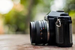 An old black film camera against a blurry green leaf background. photo