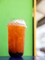 Orange iced tea in a clear plastic cup is placed near a green wall. photo