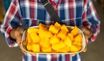 A close-up view of yellow papaya slices piled up in a white plate that is held in the hands. photo