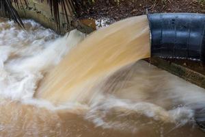 una vista de primer plano del agua que fluye violentamente de una tubería de acero cerca de la orilla de hormigón. foto