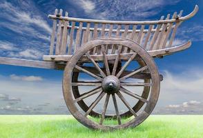 Side of an old wooden cart on grass with sky clouds. photo