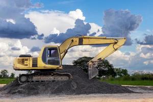 A view of an old yellow backhoe stationary on a black stone mound . photo