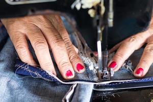 reparación de jeans de costura a mano de uñas rojas. foto