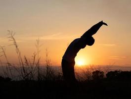 silueta de la puesta de sol con la espalda del hombre estirando el cuerpo. foto