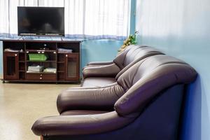 Three brown sofa armchairs in a blue wall room with flat screen TV and light through curtains. photo