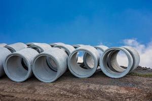 A low angle view of large concrete pipes lined up on the ground beside the road. photo