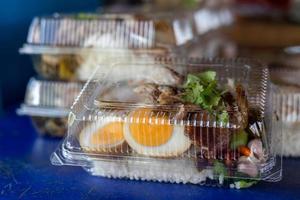 Close-up side view of pork leg rice in a clear plastic box. photo