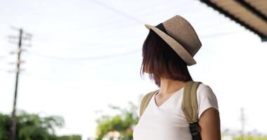 vista laterale della giovane donna asiatica felice del viaggiatore con il cappello che cammina e che riposa per l'acqua potabile alla stazione ferroviaria. donna assetata che beve acqua. concetto di trasporto, viaggio e bevande. video