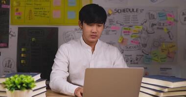 un homme d'affaires asiatique professionnel est assis au bureau avec un ordinateur portable travaillant au bureau. il reçoit une excellente nouvelle et est ravi. homme souriant et bras croisés. concept de démarrage et d'entrepreneur. video