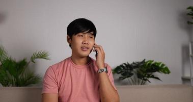Portrait of Smiling Asian calling a person.Young man listening and talking with smartphone in home living room. Relaxed man speacking on mobile phone device. Discussing with friend family.