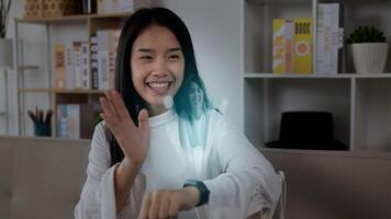 Close up of Asian woman pressing buttons on smart watch while sitting on sofa. Projecting visible AR screen and chatting on video call. Futuristic and technological concept.