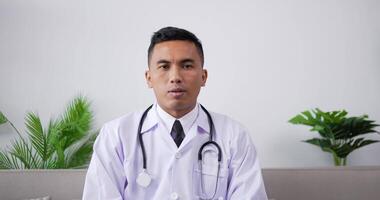 Asian doctor talking to patient making video call on laptop while sitting on sofa. Professional physician speaking looking at camera by webcam in web chat consulting client online.Telemedicine concept