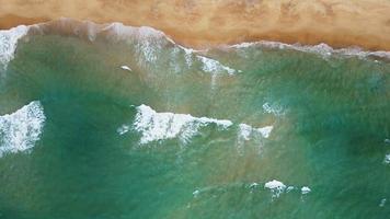 Aerial view of white sand beach and water surface texture. Foamy waves with sky. Beautiful tropical beach. Amazing Sandy coastline with white sea waves. Nature, seascape and summer concept. Zoom in.