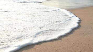 playa de arena oceánica y textura de la superficie del agua. olas espumosas con cielo y nubes. hermosa playa tropical. increíble costa de arena con olas de mar blanco. concepto de naturaleza, paisaje marino y verano. video