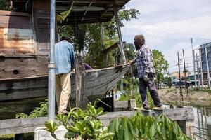 un grupo de trabajadores tailandeses está instalando grandes eslingas de cuerda para levantar y mover un viejo bote de madera.