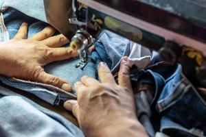 A close up hand is repairing the jeans with an old sewing machine. photo