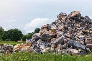 pilas de granito cerca de la hierba, malezas, retroexcavadora lejana. foto