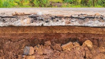 la capa de suelo ha sido erosionada bajo el camino rural pavimentado. foto