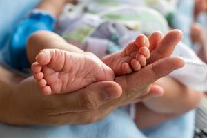 Both feet of a newborn baby child and female hand.