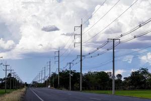 vista de campos de arroz verde con postes de electricidad en la carretera y nubes nubladas. foto