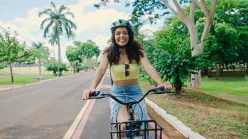 Young Latin woman in protective helmet is riding her bicycle along the bike path in a city park photo
