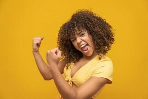 joven hermosa morena de cabello rizado felizmente regocijándose diciendo sí con fondo amarillo. concepto de éxito y logro. mujer bonita alegre sobre fondo amarillo. foto