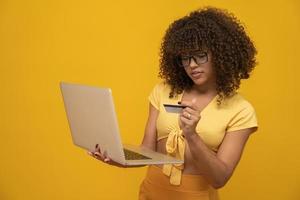 Young beautiful curly hair girl with laptop and credit card on yellow background, business woman shopping online. photo