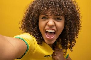 Brazil supporter. Brazilian woman fan celebrating on soccer football match on yellow background. Brazil colors. photo