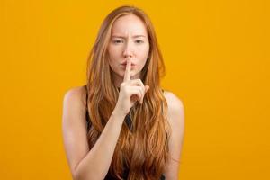 Close up of a beautiful amazing she her foxy lady hold arm hand index finger mouth lips ask stop talking tell speak say secrecy information on yellow background. photo