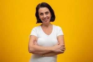 Attractive middle aged woman with folded arms on yellow background photo