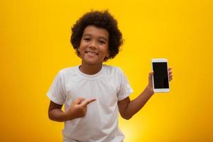 niño emocionado sonriendo y apuntando a la pantalla blanca en el teléfono inteligente. foto