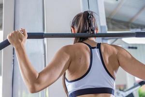 Athletic woman using machine for pumping back muscles in gym, back view photo