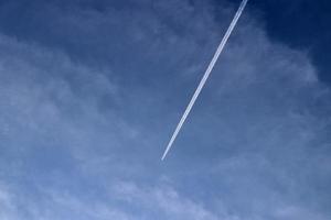 Aircraft condensation contrails in the blue sky inbetween some clouds photo