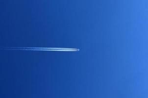 Aircraft condensation contrails in the blue sky inbetween some clouds photo