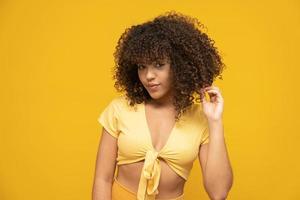 Happy laughing American African woman with her curly hair on yellow background. Laughing curly woman in sweater touching her hair and looking at the camera. photo