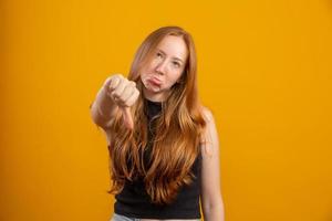 Unhappy redhead woman giving thumbs down gesture looking with negative expression and disapproval. Yellow background. photo