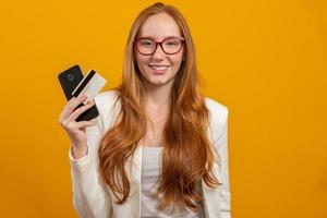 Young, confident, successful and beautiful business redhead woman buying with the smartphone on yellow. Occupation, career, job concept. photo