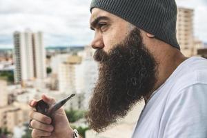 elegante hombre barbudo fumando pipa mirando el horizonte desde lo alto de un edificio alto. foto