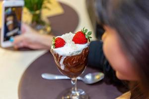 mujer tomando fotos de deliciosos helados mezclas blancas de fresa con un teléfono inteligente.