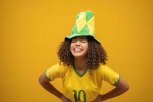Brazil supporter. Brazilian woman fan celebrating on soccer football match on yellow background. Brazil colors. photo