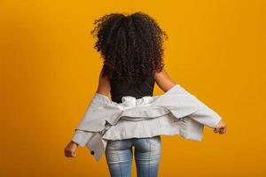 Young black woman on her back with afro hairstyle on yellow background. Girl with african hairstyle. Studio shot. photo