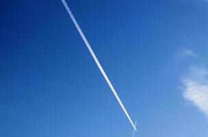 Aircraft condensation contrails in the blue sky inbetween some clouds photo