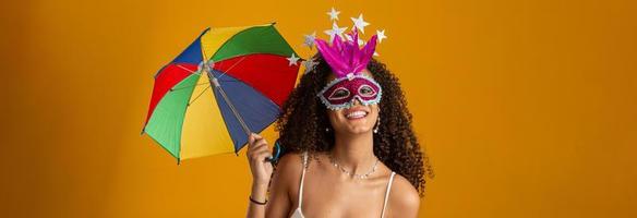 mujer joven de pelo rizado celebrando la fiesta del carnaval brasileño con paraguas frevo en amarillo.