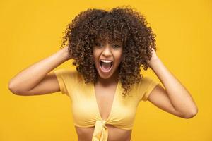 feliz risa mujer africana americana con su pelo rizado sobre fondo amarillo. mujer rizada riendo en suéter tocando su cabello y mirando a la cámara. foto