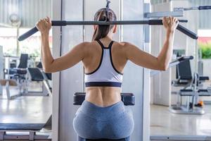 mujer atlética que usa una máquina para bombear los músculos de la espalda en el gimnasio, vista trasera foto