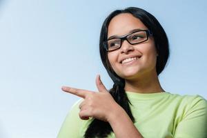 joven estudiante morena con gafas apuntando hacia el lado y sonriendo. foto