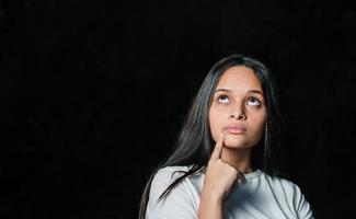 joven estudiante adolescente hermosa chica soñando pensando mirando de lado sobre fondo oscuro. foto