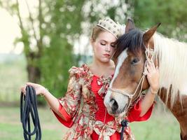 A beautiful western woman in a beautiful dress stands with her horse in the wild west photo